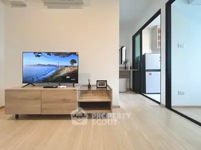 Modern living room with wooden flooring and sleek TV stand, leading to a bright kitchen area.