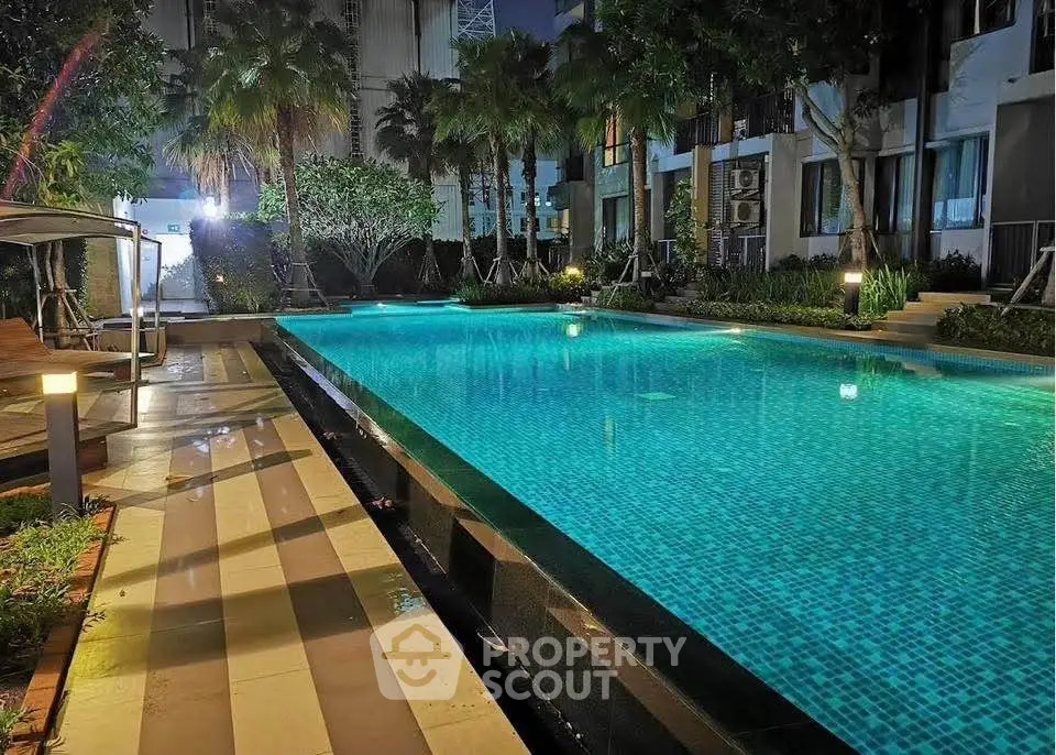 Luxurious condominium pool area with ambient lighting and lush greenery at night.