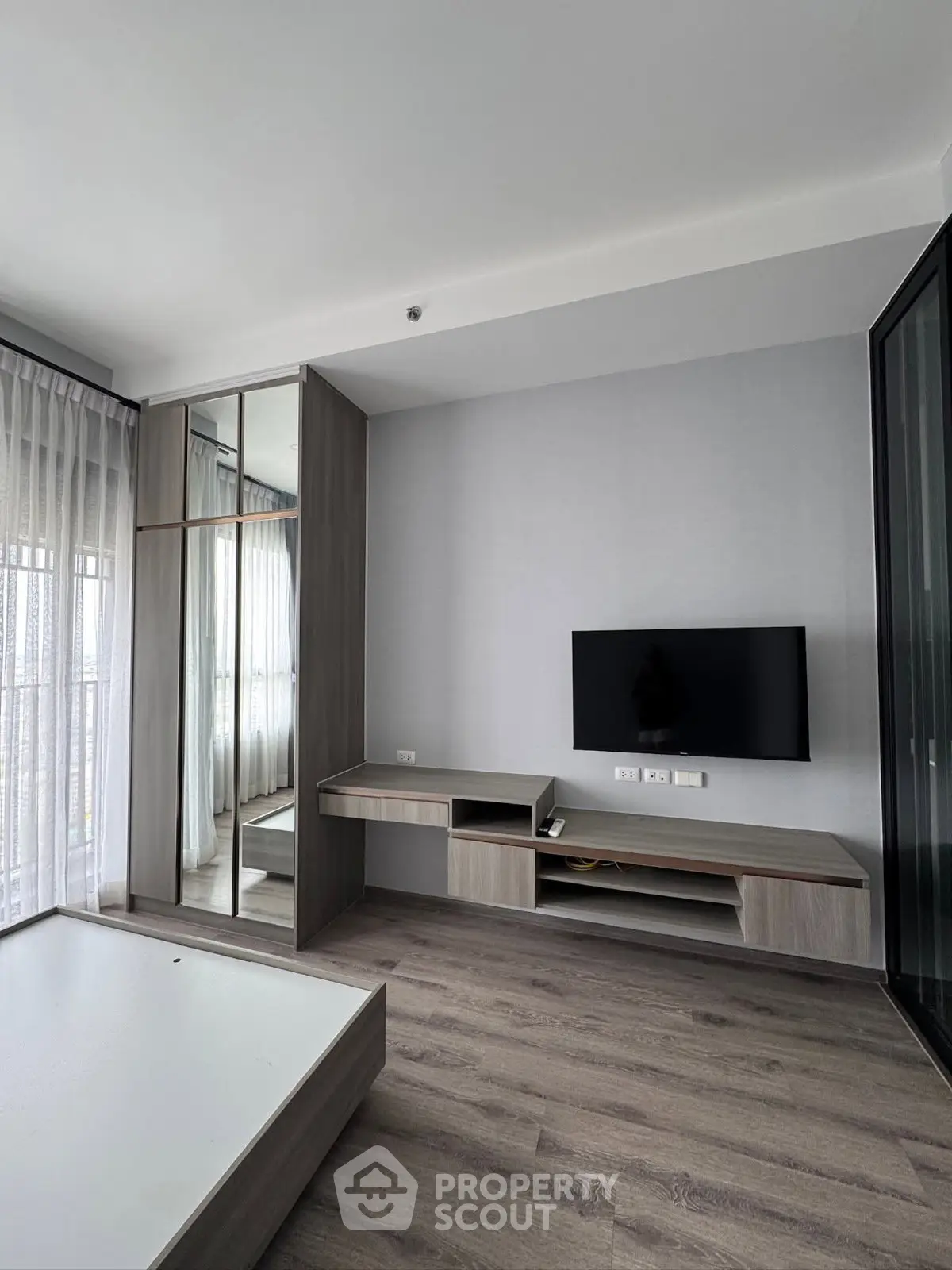 Modern living room with sleek furniture and mounted TV, featuring floor-to-ceiling windows and stylish wood flooring.