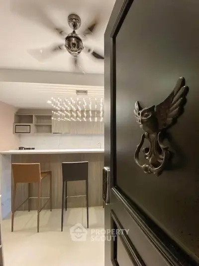 Modern kitchen with stylish bar stools and elegant lighting, viewed through an ornate door.