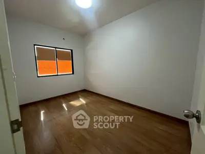 Spacious empty room with wooden flooring and window, ideal for customization.