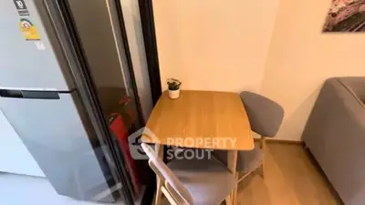 Cozy dining nook with wooden table and chairs beside modern fridge in compact apartment.