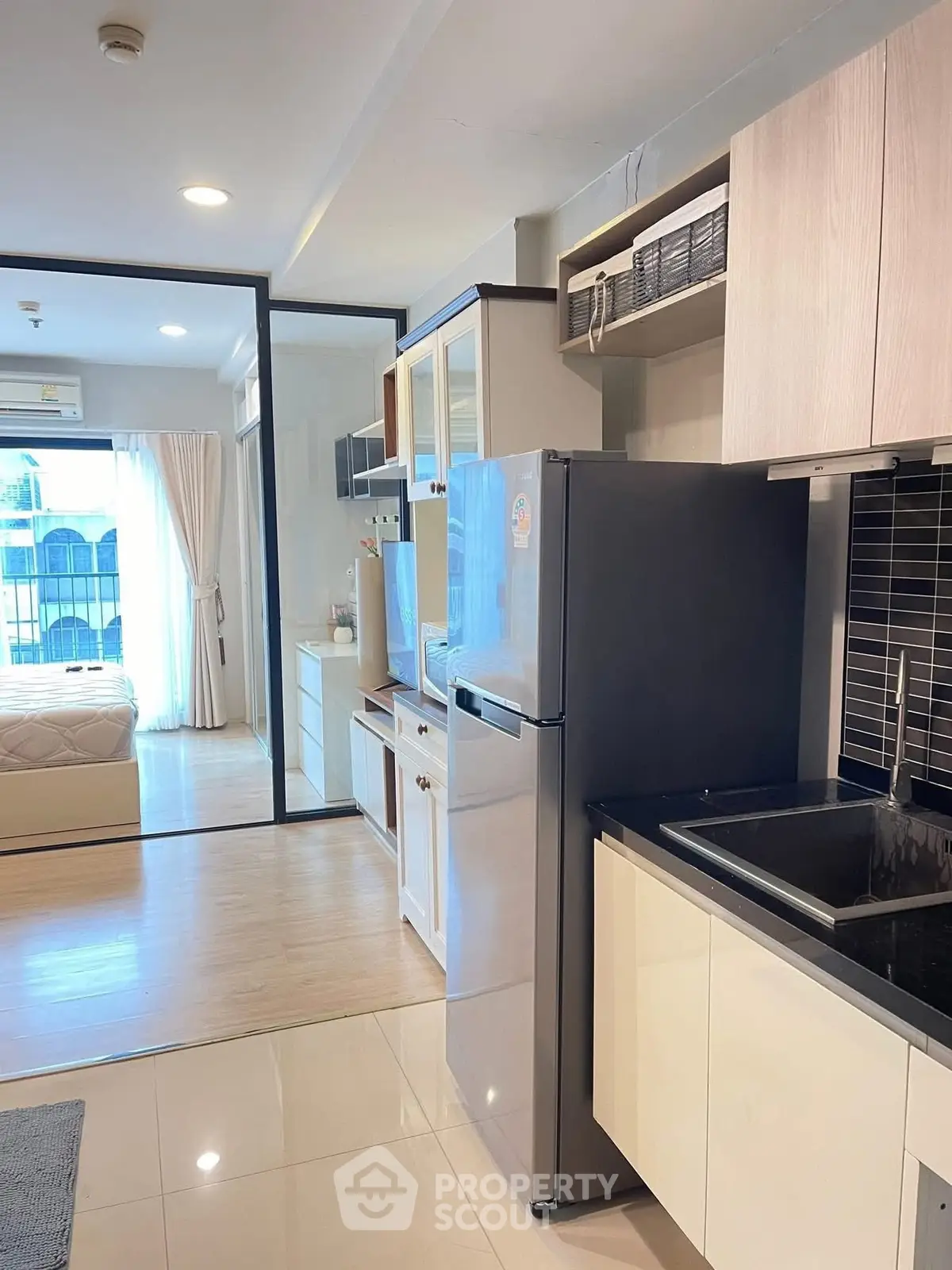 Modern apartment kitchen with sleek appliances and open layout leading to a cozy bedroom.