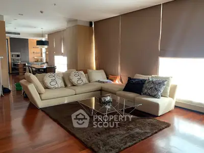 Spacious modern living room with elegant sofa and glass coffee table, featuring open layout to kitchen area.