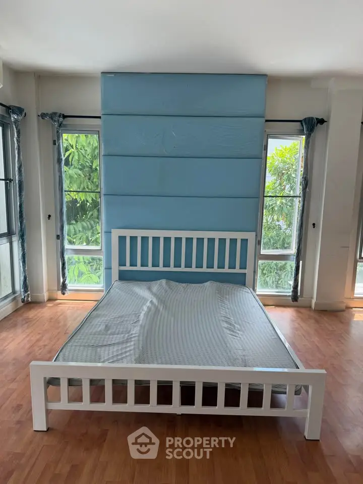 Spacious bedroom with large windows and wooden flooring, featuring a modern bed frame and serene blue accent wall.