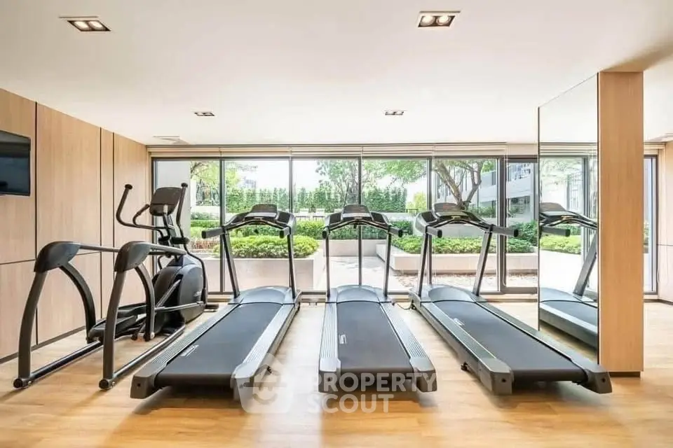 Modern gym with treadmills and garden view in luxury apartment complex.