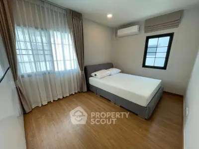 Modern bedroom with wooden flooring and large windows, featuring a cozy bed and air conditioning.