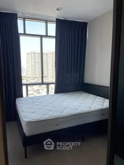 Modern bedroom with large window and city view, featuring a comfortable bed and dark curtains.
