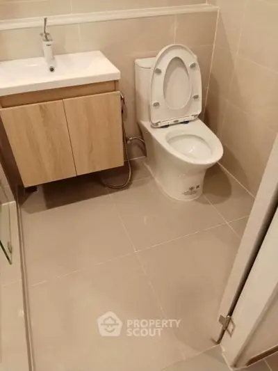 Modern bathroom with sleek fixtures and neutral tiles, featuring a compact vanity and toilet.