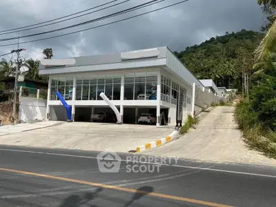 Modern commercial building with large glass facade and ample parking space, set against a lush hillside backdrop.