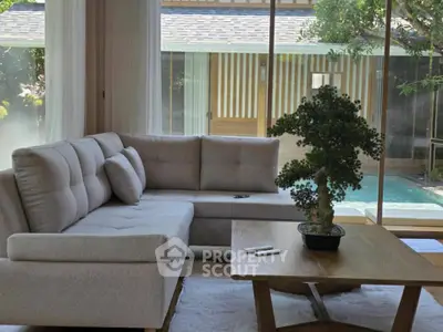 Chic living room with modern sofa overlooking serene pool and lush greenery.