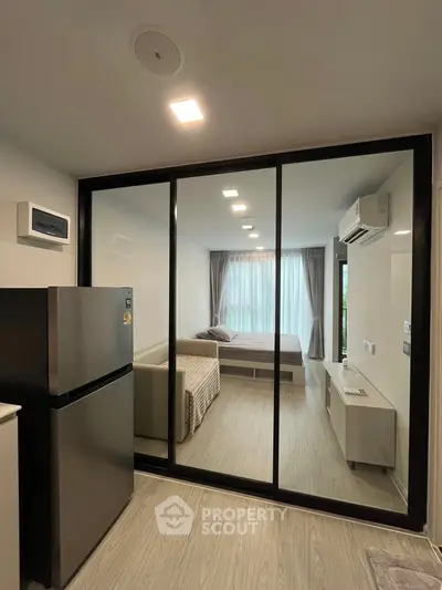 Modern studio apartment with glass partition, featuring a cozy bedroom and sleek kitchen area.