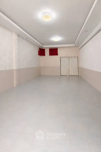 Spacious empty room with tiled flooring and elegant ceiling lights, perfect for versatile use.
