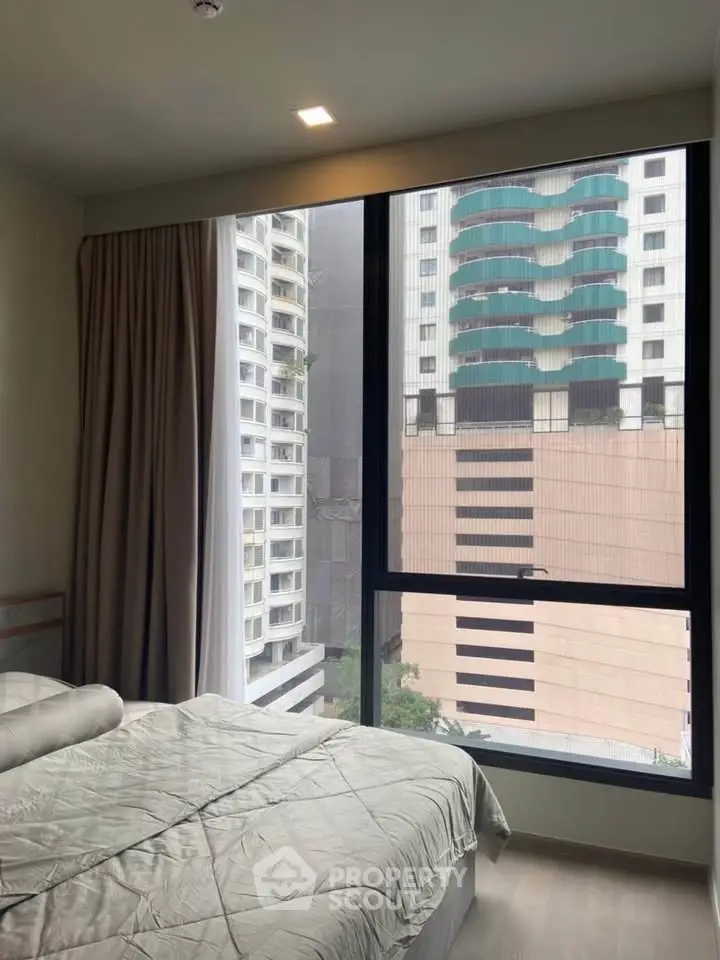 Modern bedroom with large window offering cityscape view in high-rise apartment.