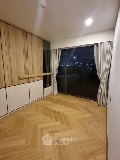 Elegant bedroom with wooden flooring and city view through large window.