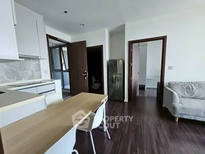 Modern apartment interior with open kitchen and cozy living area, featuring sleek furniture and wooden flooring.