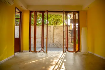 Spacious room with large wooden folding doors opening to a private patio, featuring vibrant yellow walls and tiled flooring.