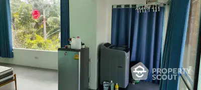 Bright laundry room with washing machine, fridge, and large windows overlooking lush greenery.