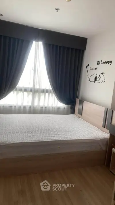Cozy bedroom with wooden flooring and Snoopy wall art, featuring a large window with dark curtains.