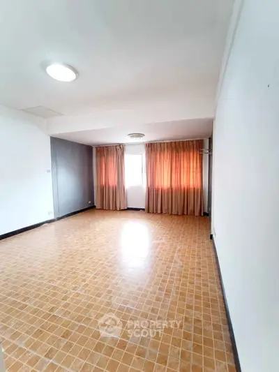 Spacious empty room with tiled floor and large window with curtains.