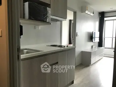 Modern apartment interior with compact kitchen and cozy living area, featuring sleek cabinetry and natural light.