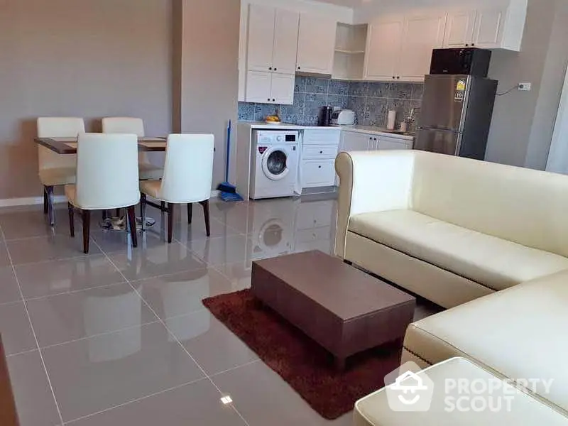 Modern open-plan living room with sleek kitchen and dining area, featuring white furniture and tiled flooring.