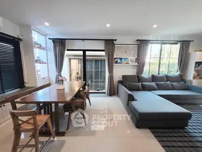 Spacious living room with modern gray sectional sofa and dining area, featuring large windows for natural light.