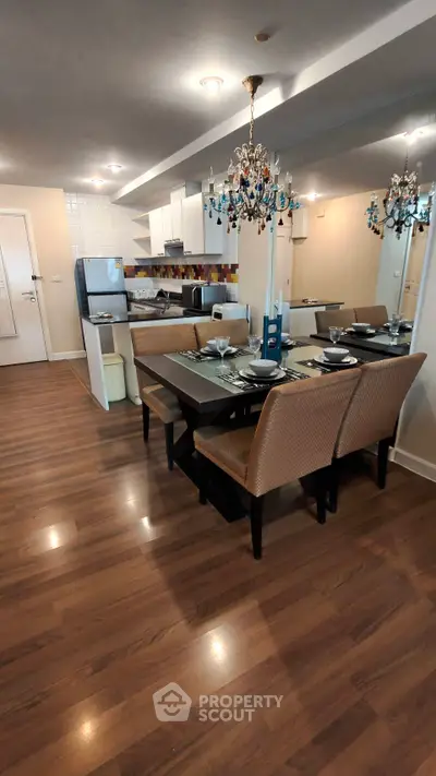 Modern open-layout kitchen and dining area with elegant chandelier and wooden flooring.