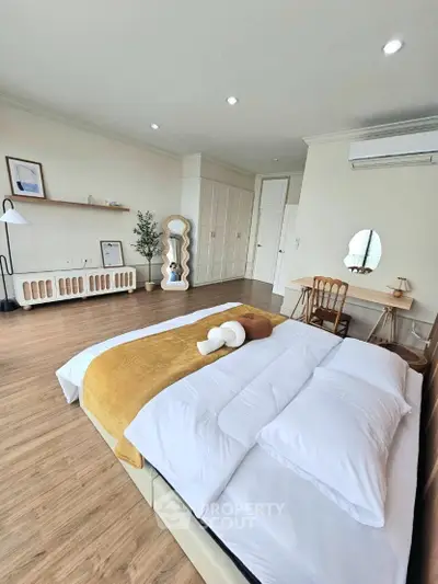 Spacious bedroom with modern decor and natural light, featuring wooden flooring and stylish furnishings.