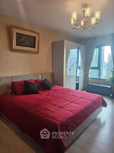 Luxurious bedroom with red bedding, elegant chandelier, and city view window in modern apartment.