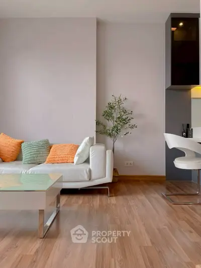 Modern living room with stylish decor and wooden flooring, featuring a sleek white sofa and vibrant cushions.