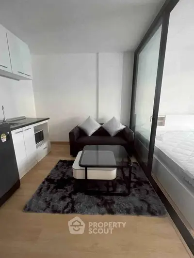 Modern studio apartment with sleek kitchen and cozy living area, featuring glass partition and stylish decor.