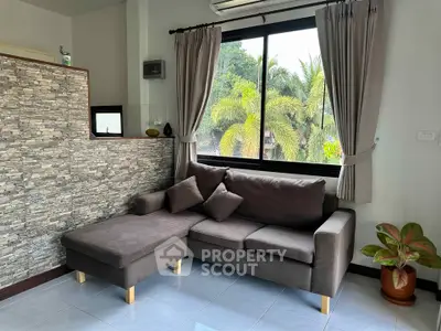 Cozy living room with modern sofa and large window view of lush greenery.