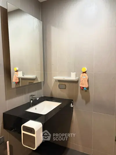 Modern bathroom with sleek sink and mirror, featuring stylish tile design and contemporary fixtures.