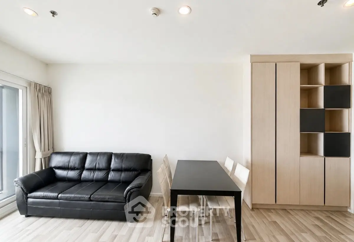 Modern living room with sleek black sofa and dining area in minimalist apartment.
