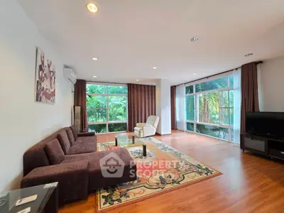 Spacious living room with large windows and lush garden view, featuring modern furniture and elegant decor.