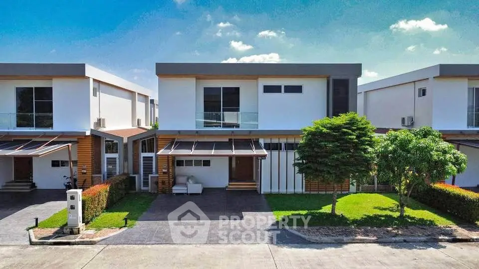 Modern two-story house with sleek design, large windows, and lush green lawn in a suburban neighborhood.