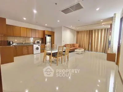 Spacious open-plan living room with modern kitchen and dining area, featuring sleek appliances and elegant furnishings.
