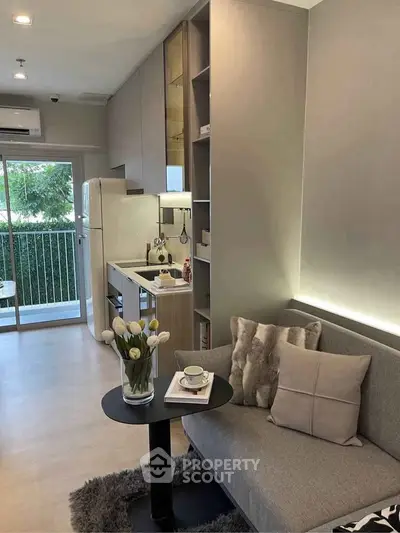 Modern living room with cozy sofa, compact kitchen, and balcony view in stylish apartment.
