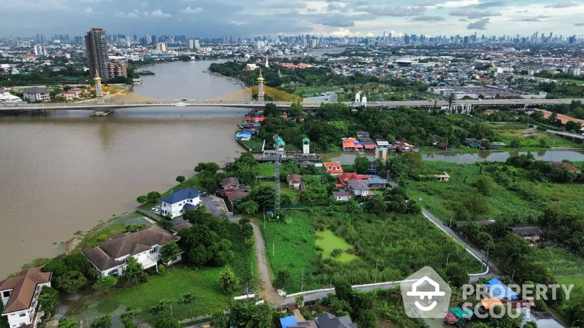 Stunning aerial view of riverside properties with lush greenery and city skyline in the background.