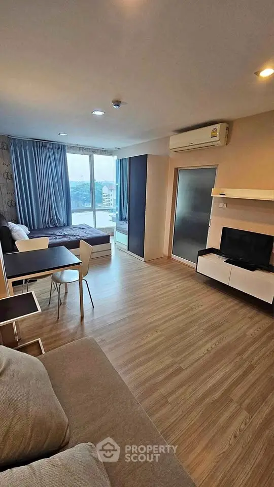 Modern studio apartment with open layout and large windows offering city views.