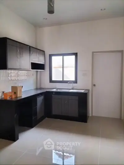 Modern kitchen with sleek black cabinetry and large window for natural light.