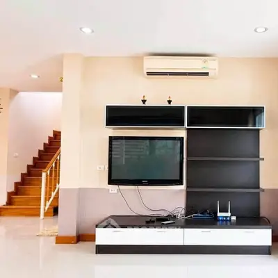 Modern living room with sleek TV unit and staircase, featuring air conditioning and stylish decor.