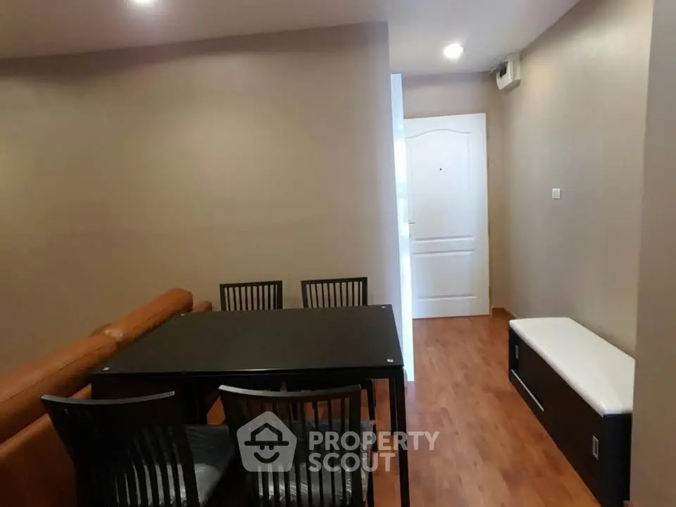 Modern dining area with sleek black table and chairs, adjacent to cozy living space with wooden flooring.
