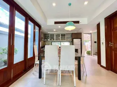 Modern dining area with glass table, stylish chairs, and open kitchen layout in a bright, airy space.
