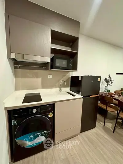 Modern compact kitchen with washing machine, microwave, and fridge in stylish apartment.