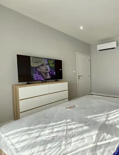 Modern bedroom with sleek furniture and wall-mounted TV, featuring a minimalist design and air conditioning.
