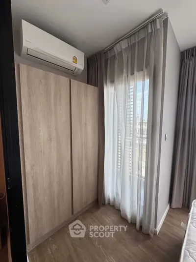 Cozy bedroom corner with wardrobe and air conditioning, featuring floor-to-ceiling windows with sheer curtains.