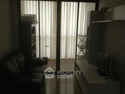 Cozy living room with leather sofa and TV, featuring floor-to-ceiling windows with sheer curtains.