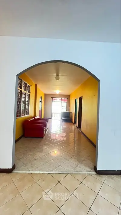 Spacious living room with vibrant yellow walls and red sofa, featuring tiled flooring and ample natural light.